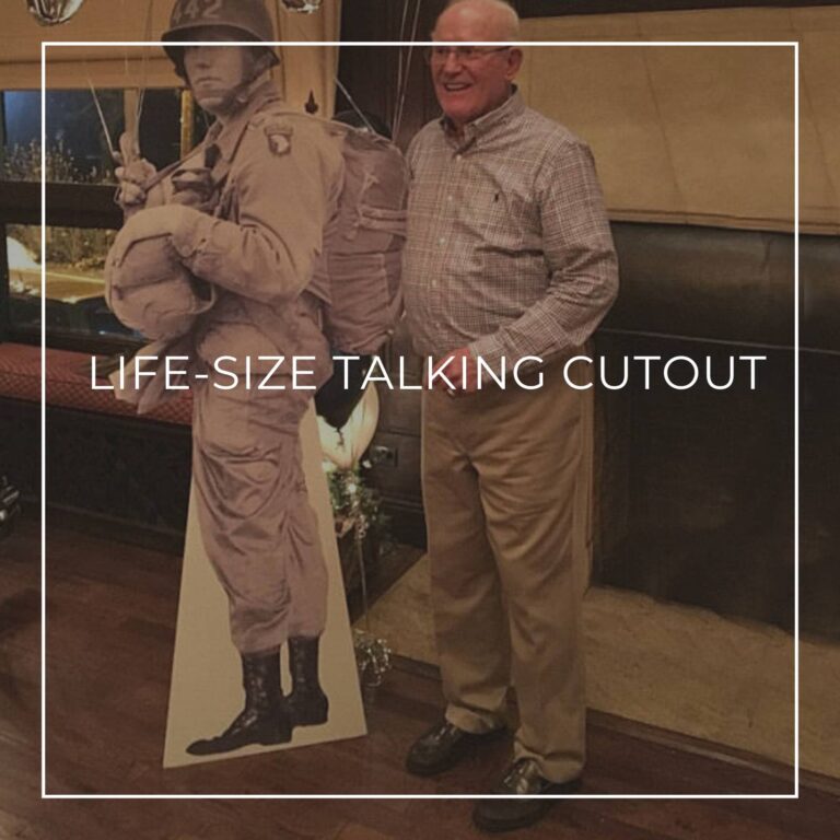 80 year old man standing next to a life-size cutout standee of his younger self as a soldier