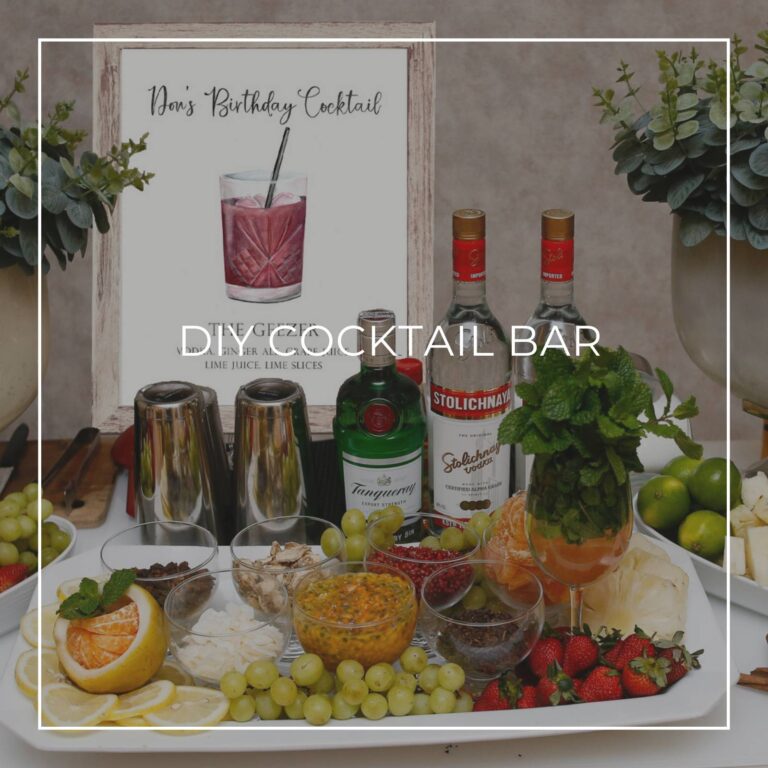 DIY cocktail bar with liquor, ingredients, and a cocktail recipe sign for party guests to make their own drink