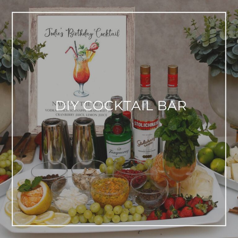 DIY cocktail bar with liquor, ingredients, and a cocktail recipe sign for party guests to make their own drink