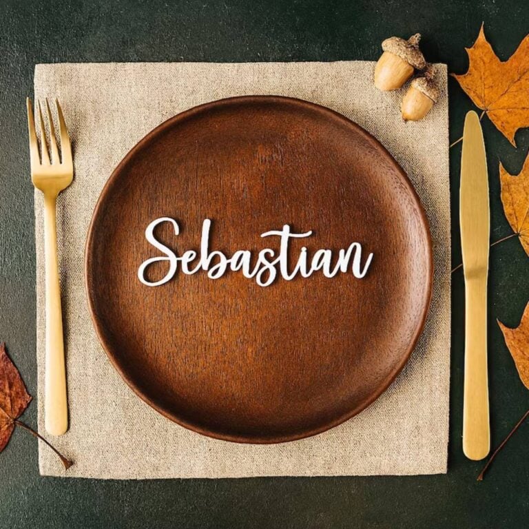 White 3D script name Sebastian on a dark wooden plate with gold cutlery and autumn leaves