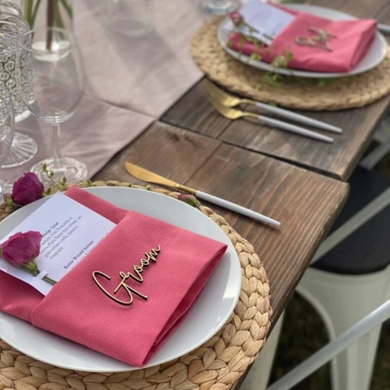 Wooden script place card reading Groom on a pink napkin at a rustic wedding table