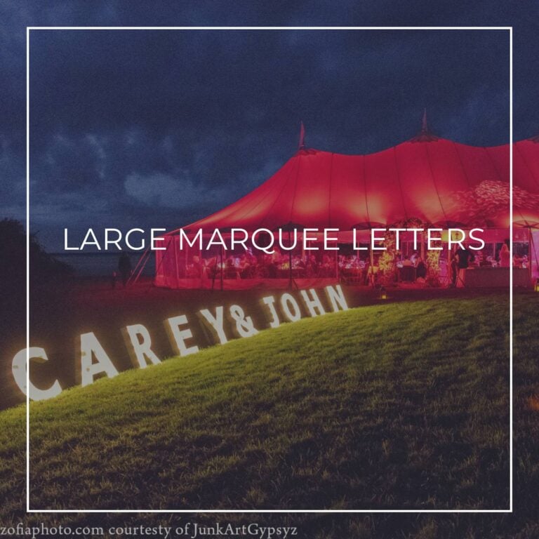 large custom marquee letters spelling 'Carey & John' set up on grass outside party tent lit red at night