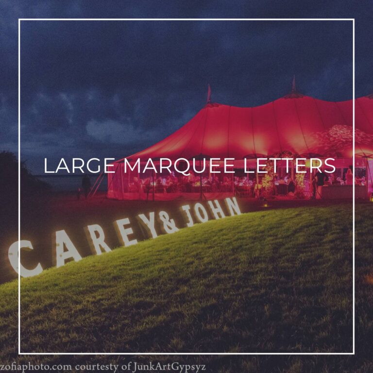 large custom marquee letters spelling 'Carey & John' set up on grass outside party tent lit red at night