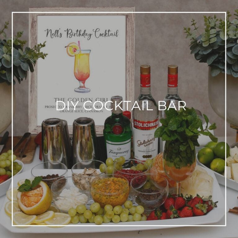 DIY cocktail bar with liquor, ingredients, and a cocktail recipe sign for party guests to make their own drink