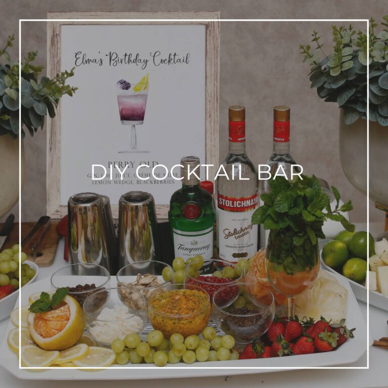 DIY cocktail bar with liquor, ingredients, and a cocktail recipe sign for party guests to make their own drink