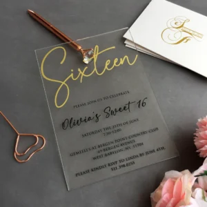 Clear acrylic invitation reading Sixteen for Olivia's Sweet 16, with a rose gold pen and paperclip