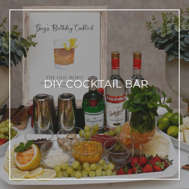 DIY cocktail bar with liquor, ingredients, and a cocktail recipe sign for party guests to make their own drink