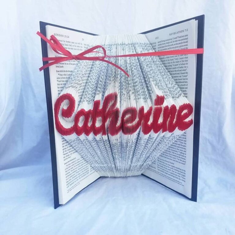 Book folding art on a Bible spelling the name “Catherine” in red, tied with a red ribbon bow