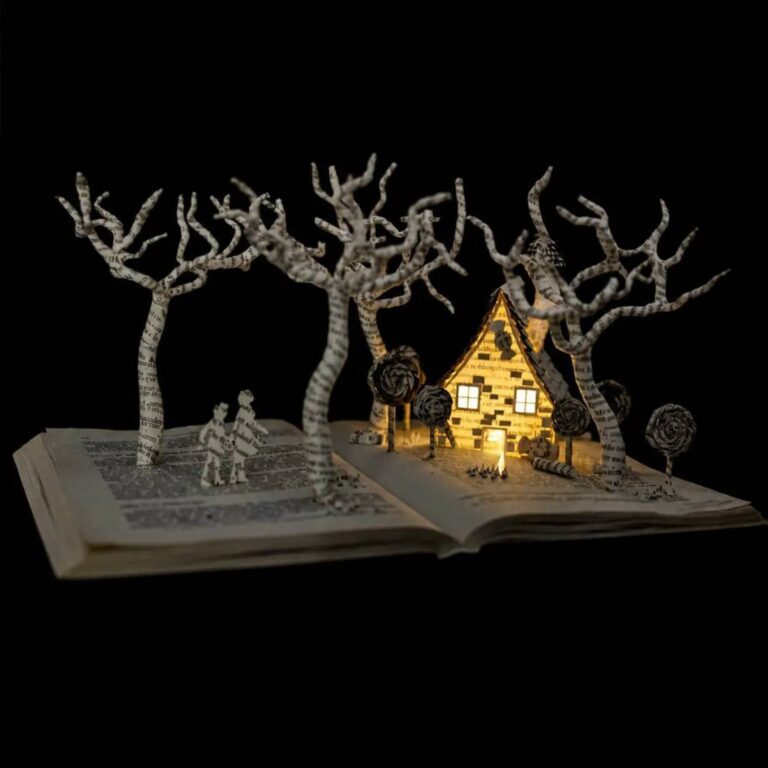 Book art scene of a lit paper cottage and bare trees with two tiny figures, on an open book