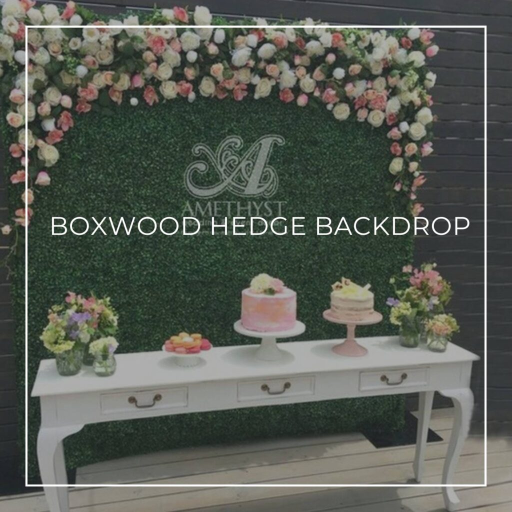 faux boxwood hedge party dessert table backdrop decorated with flowers