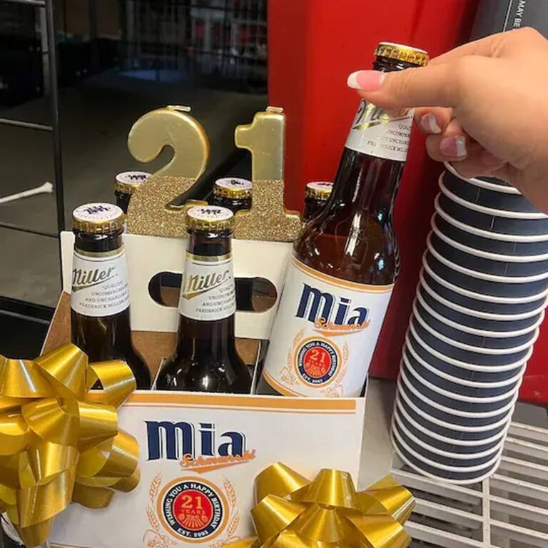 Hand lifting a Miller bottle with a custom "Mia, Wishing You a Happy Birthday, 21 Years" label from a six-pack decorated with gold "21" numbers