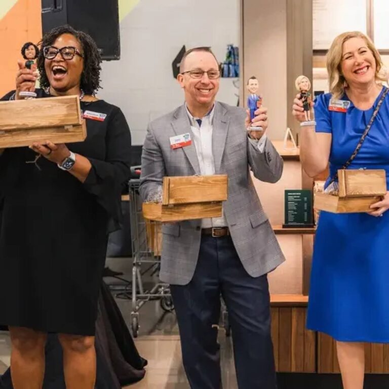 Guests at an event holding assorted custom bobbleheads and wooden gift boxes