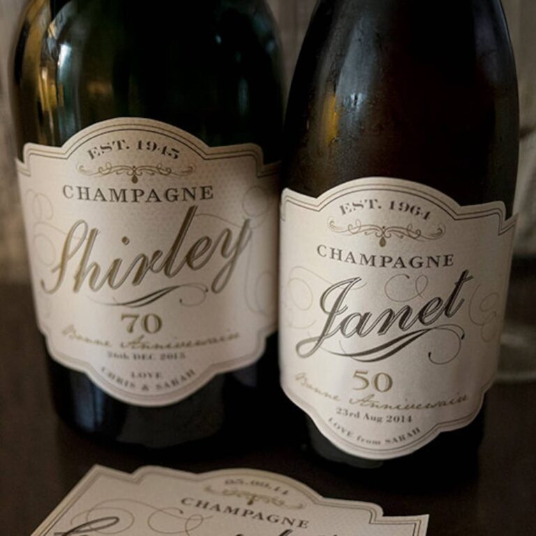 Two champagne bottles with cream vintage-style labels reading "Champagne Shirley, 70" and "Champagne Janet, 50," a spare label card in front