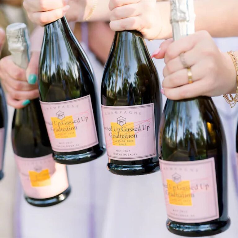 Group holding up bottles with pink "Gassed Up Graduation, Class of 2023, Tuscaloosa AL" labels marked with a yellow highlight