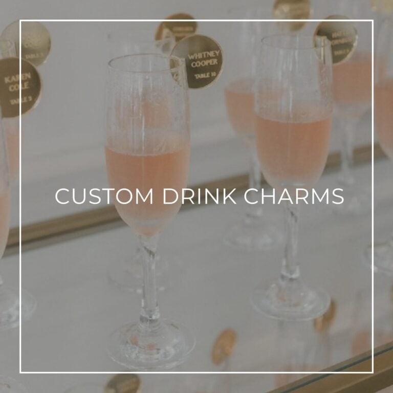 Champagne flutes with round gold place-card charms reading guest names and table numbers, labeled “Custom Drink Charms”