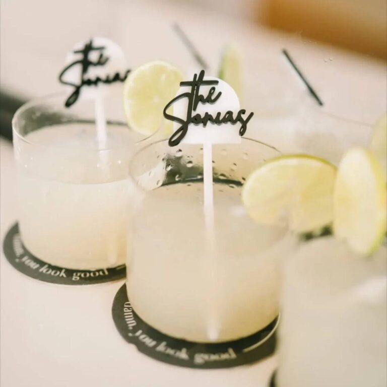 Two margaritas with white acrylic drink stirrers reading “the Sonias” in black script, garnished with lime wheels