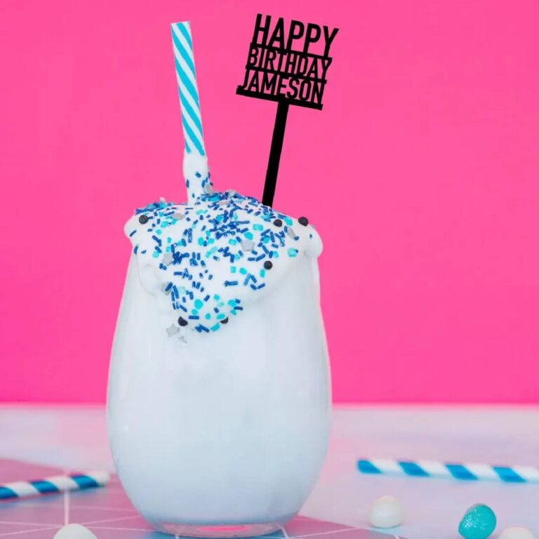 Creamy drink topped with blue sprinkles and a black acrylic sign stirrer reading “Happy Birthday Jameson” on a hot pink background