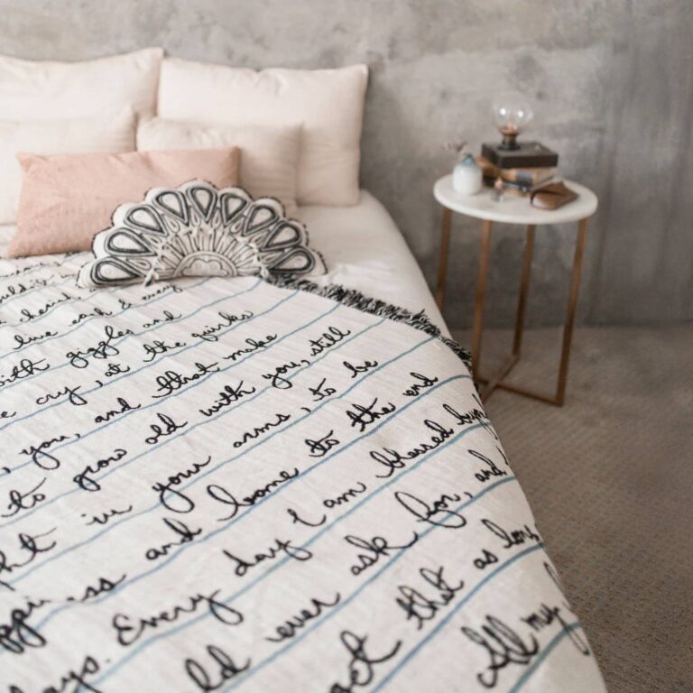 Letter blanket draped on a bed, cursive note about growing old together among pastel pillows