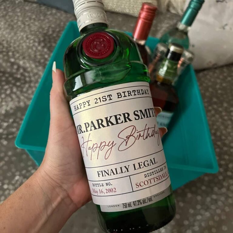 Hand holding a wax-sealed gin bottle with a "Happy 21st Birthday, Mr. Parker Smith, Finally Legal" label, more bottles in a teal bin behind it