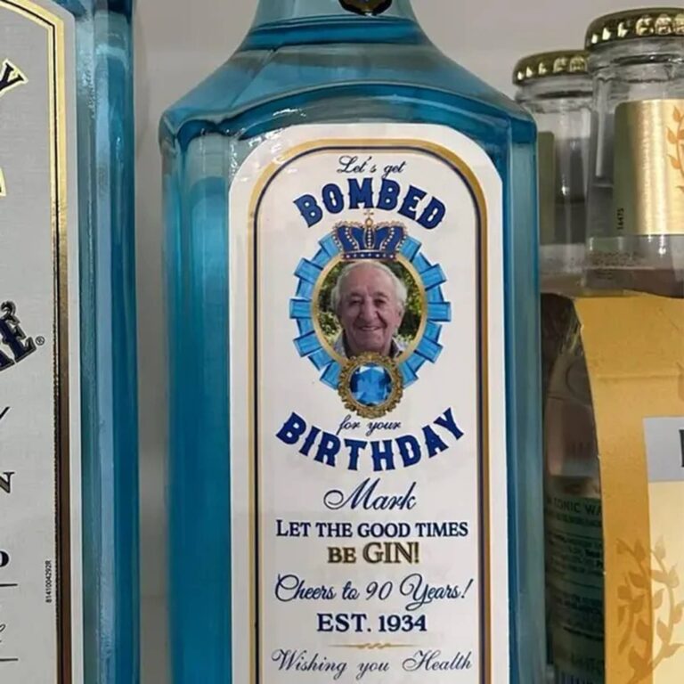 Blue gin bottle with a "Let’s Get Bombed for Your Birthday, Mark, Cheers to 90 Years! Est. 1934" label featuring a smiling older man in a ribbon medallion