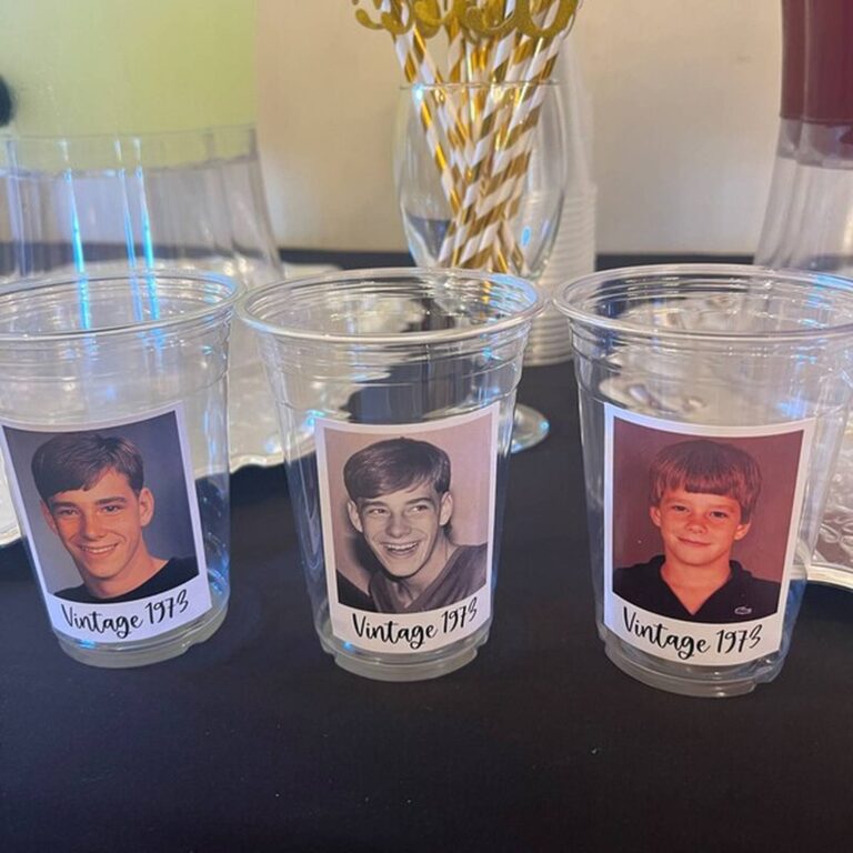 Three clear photo cups on a party table, each printed with a different boy’s yearbook photo and “Vintage 1973,” gold and white straws in the background