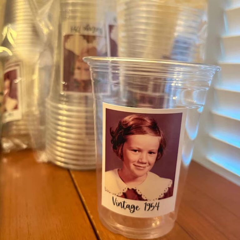 Clear photo cup on a wood table printed with a sepia childhood portrait and “Vintage 1954,” blurred matching cups behind it