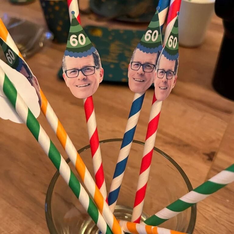 Bundle of striped photo straws topped with a bespectacled man’s face wearing green “60” party hats