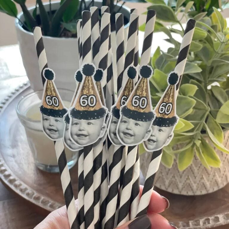 Black-and-white striped photo straws topped with a baby’s face wearing gold “60” party hats