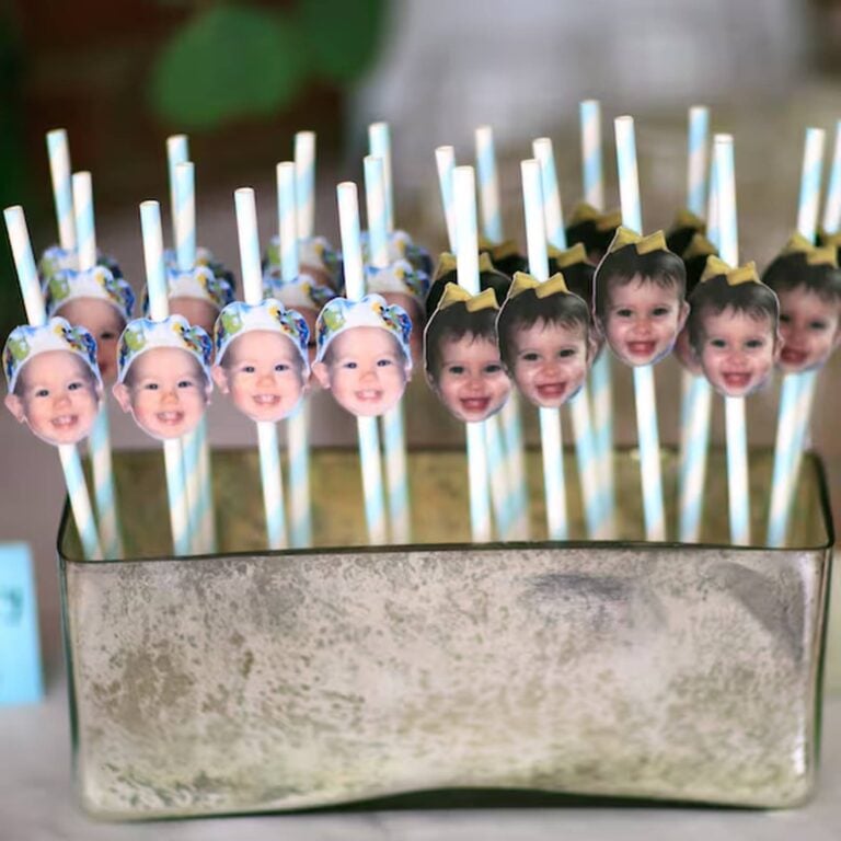 Rows of blue-and-white striped photo straws topped with two different babies’ faces in party hats, arranged in a metal planter