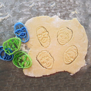 personalized custom cookie cutter of a man, woman, and 2 children's heads pressed into rolled out dough