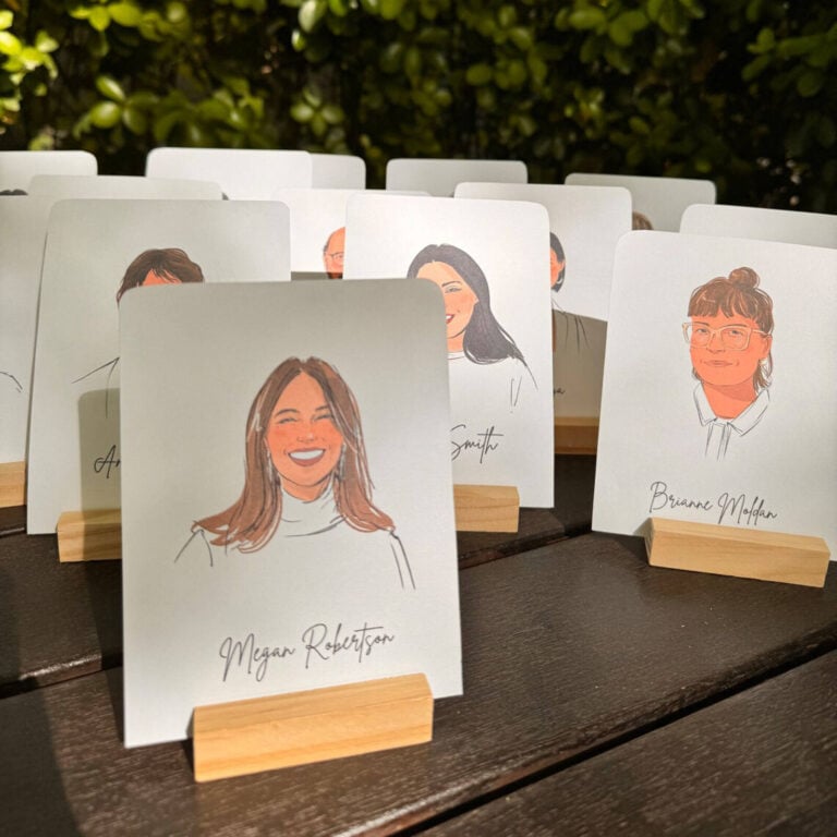 Portrait place cards on wooden stands outdoors, with Megan Robertson’s card in front