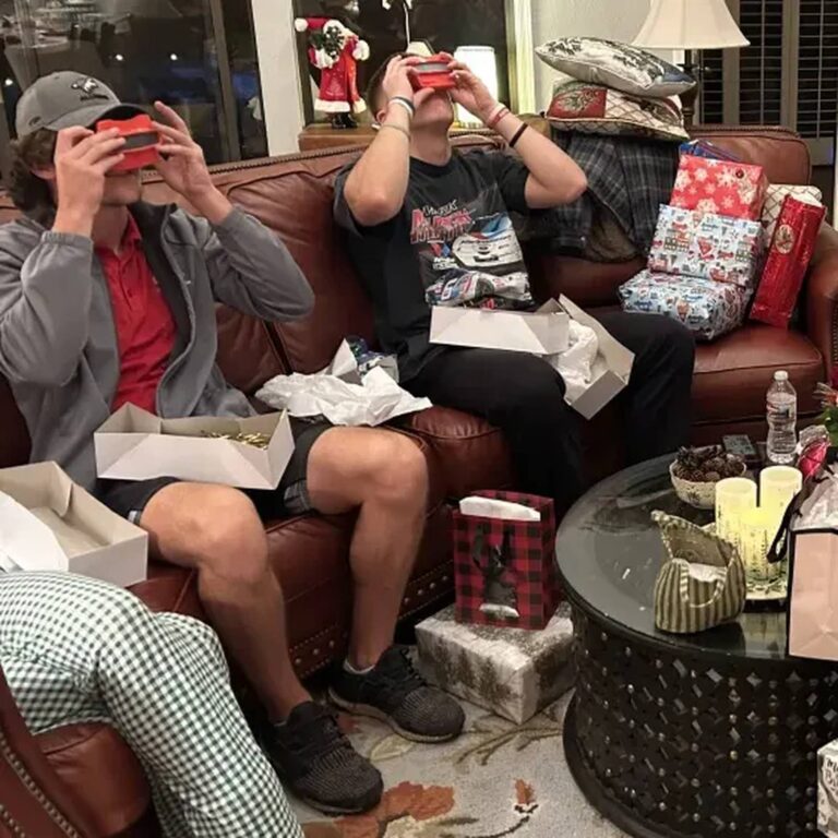 Two young men on a couch looking through red reel viewers while opening Christmas gifts