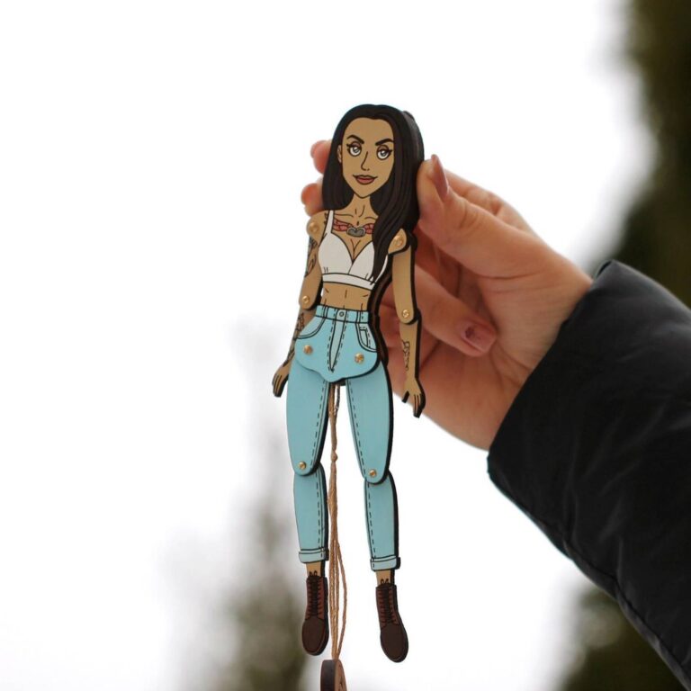 Custom wooden portrait ornament of a tattooed woman with long dark hair in a white crop top and blue jeans, held up outdoors