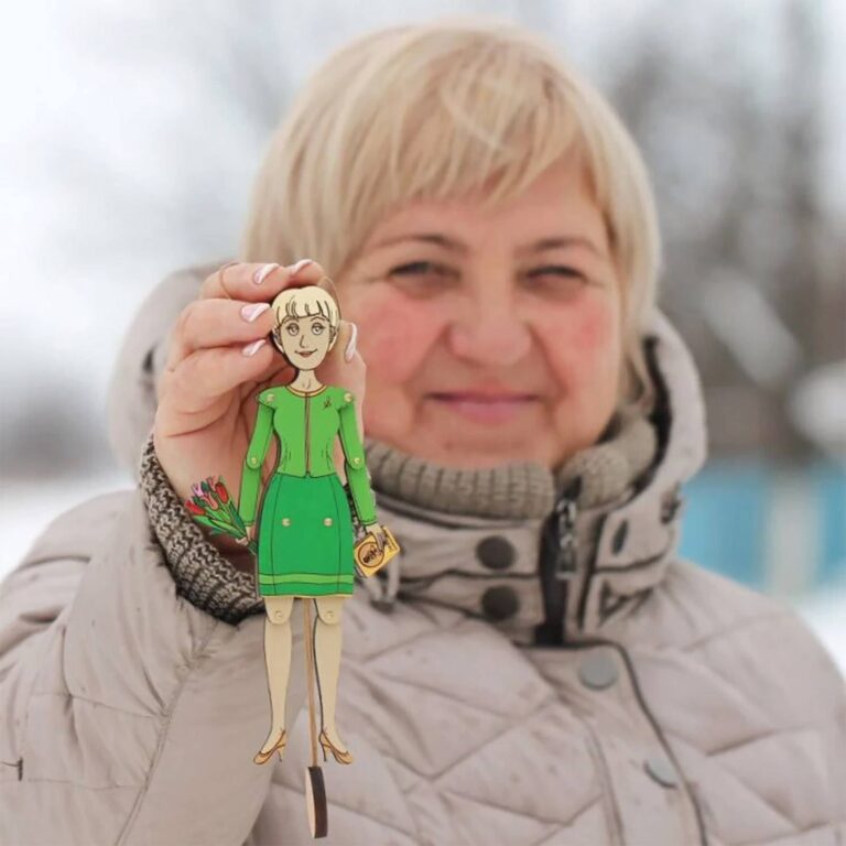 Woman smiling and holding up a custom wooden portrait ornament of herself in a green dress with tulips and a handbag