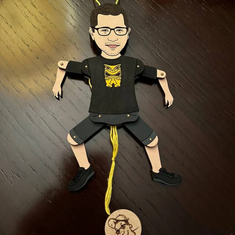 Custom wooden portrait ornament of a bearded man in a black tiki-print t-shirt and shorts, laid flat showing articulated limbs