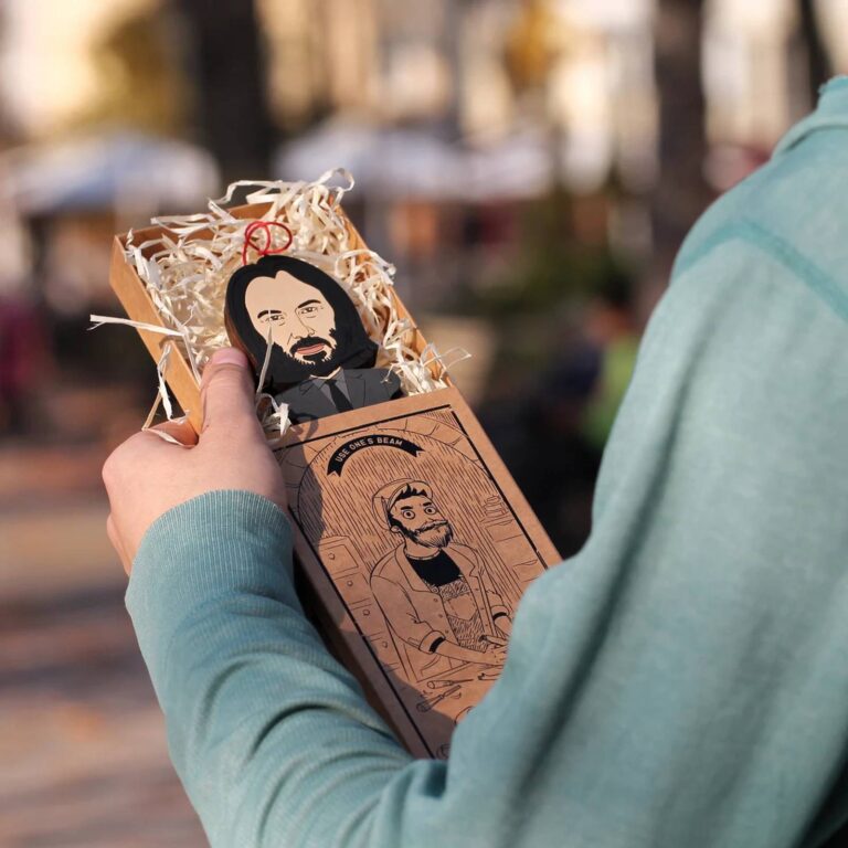 Custom wooden portrait ornament nestled in a kraft gift box with straw packing, with an illustrated character on the box lid