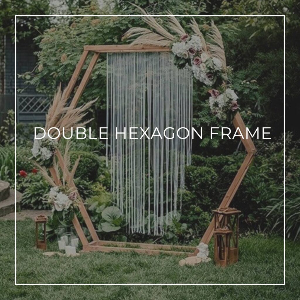 double hexagon wooden backdrop frame on a beach dressed with flowers, foliage, and lanterns