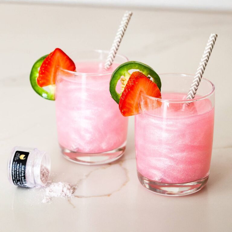 Two pink edible glitter cocktails garnished with strawberry and jalapeño slices next to a jar of Brew Glitter Soft Pink Blend