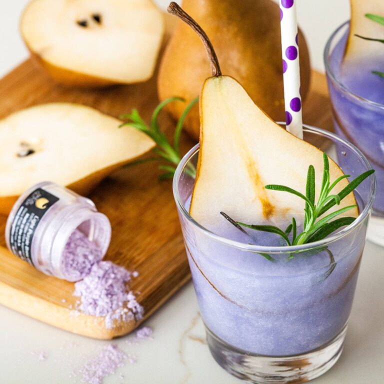Purple edible glitter cocktail garnished with a pear slice and rosemary sprig next to a jar of Brew Glitter Light Purple