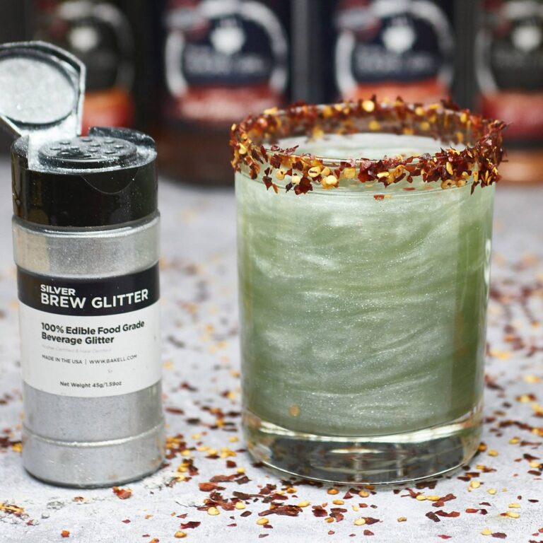 Green edible glitter cocktail with a chili flake rim next to a Silver Brew Glitter shaker