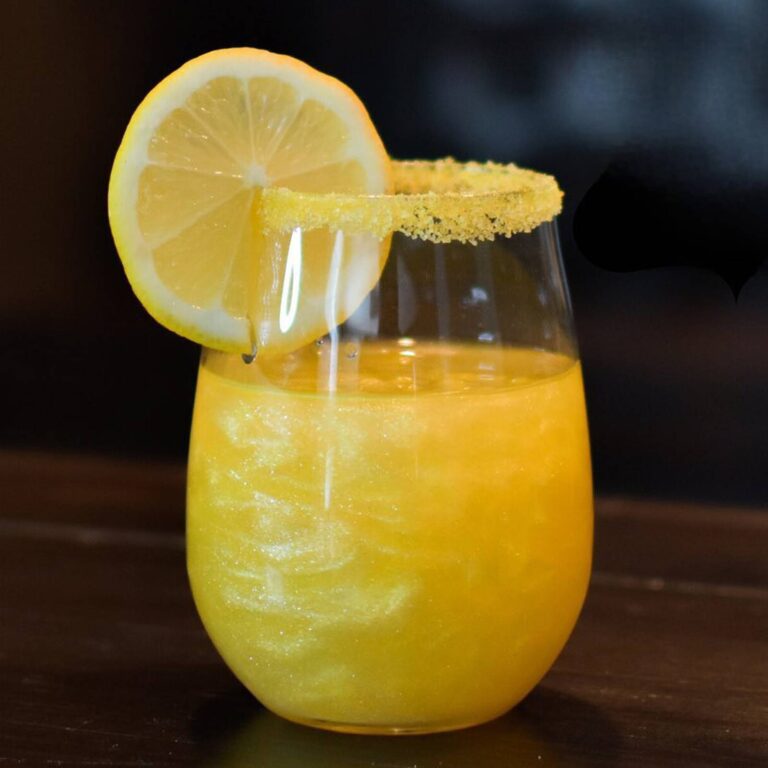 Orange edible glitter cocktail in a stemless glass with a sugared rim and lemon wheel garnish