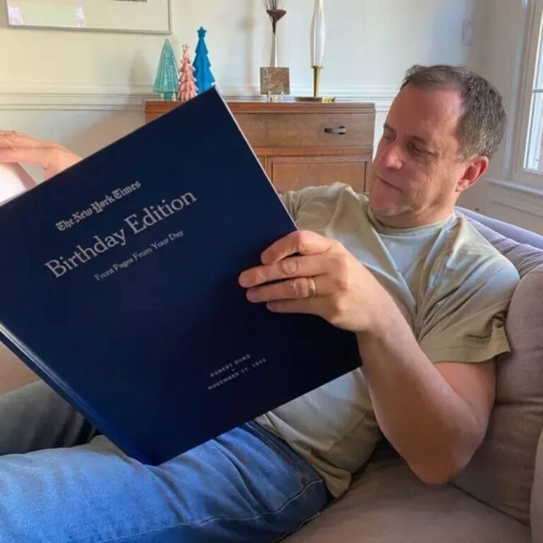 Smiling man holding his personalized New York Times Birthday Edition book with his name and birth date on the cover