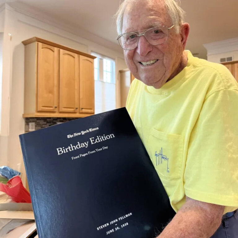 Smiling man in a yellow shirt holding his personalized New York Times Birthday Edition book
