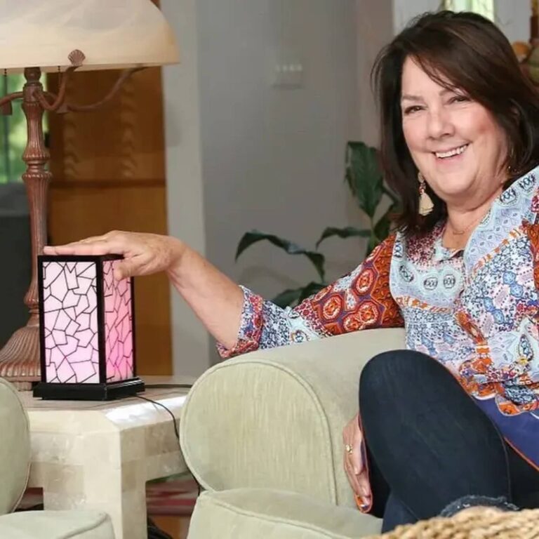 Woman on a sofa touching a pink-glowing mosaic lamp beside a traditional lamp