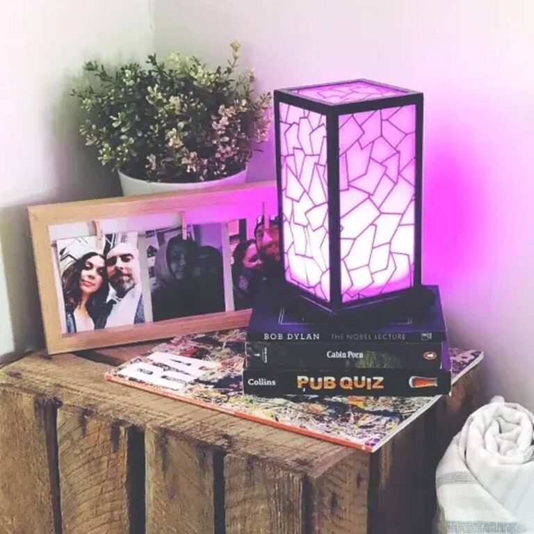 Purple-lit mosaic lamp perched on stacked books beside framed photos