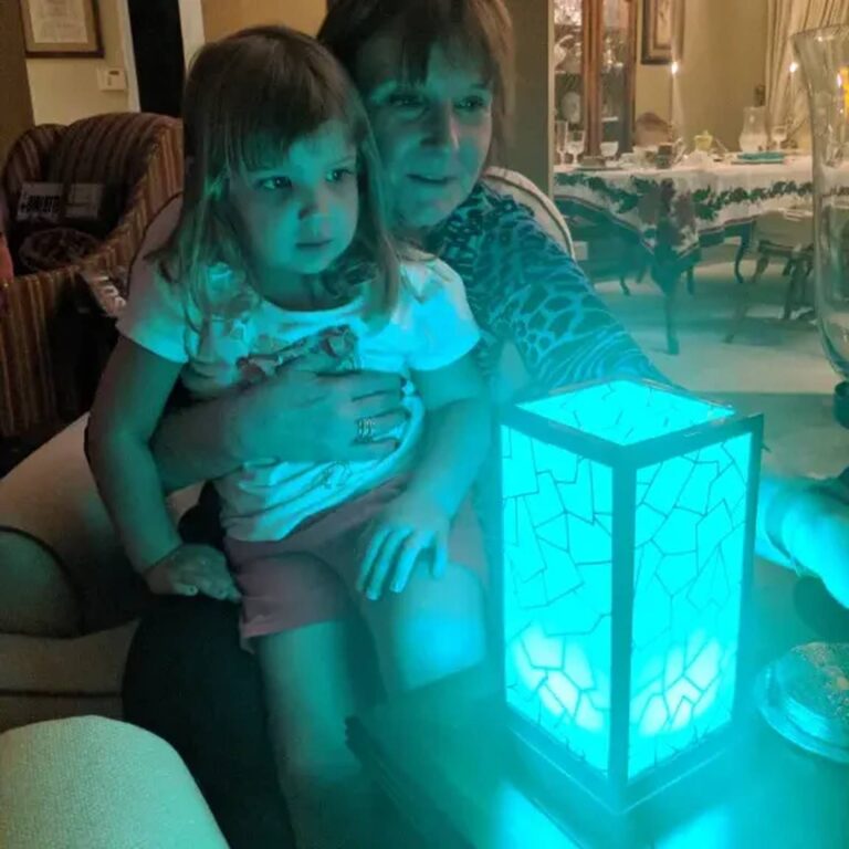 Mother and daughter beside a teal-glowing mosaic lamp at a family dinner