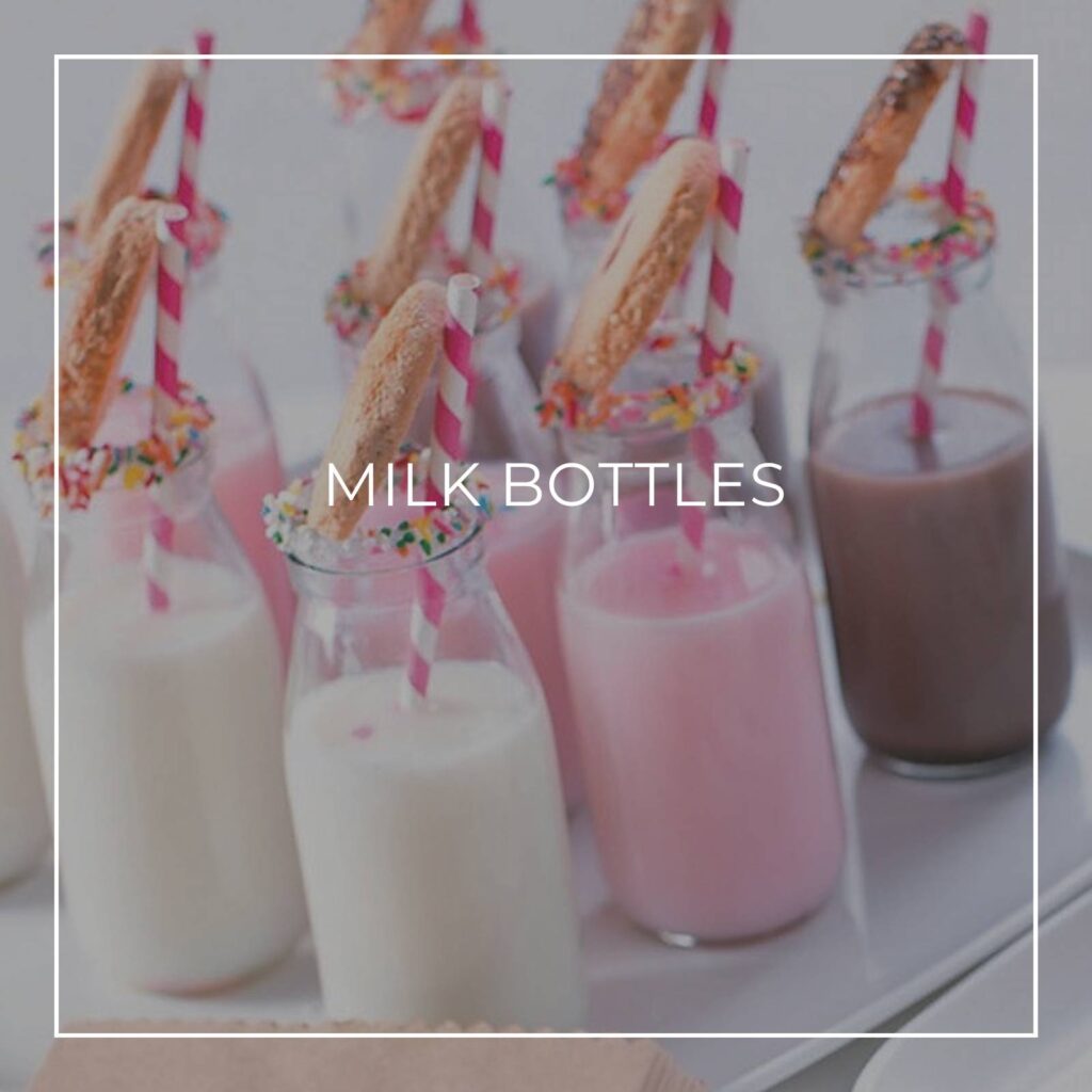milkshakes served in individual milk bottles with a cookie and straw on a party dessert table