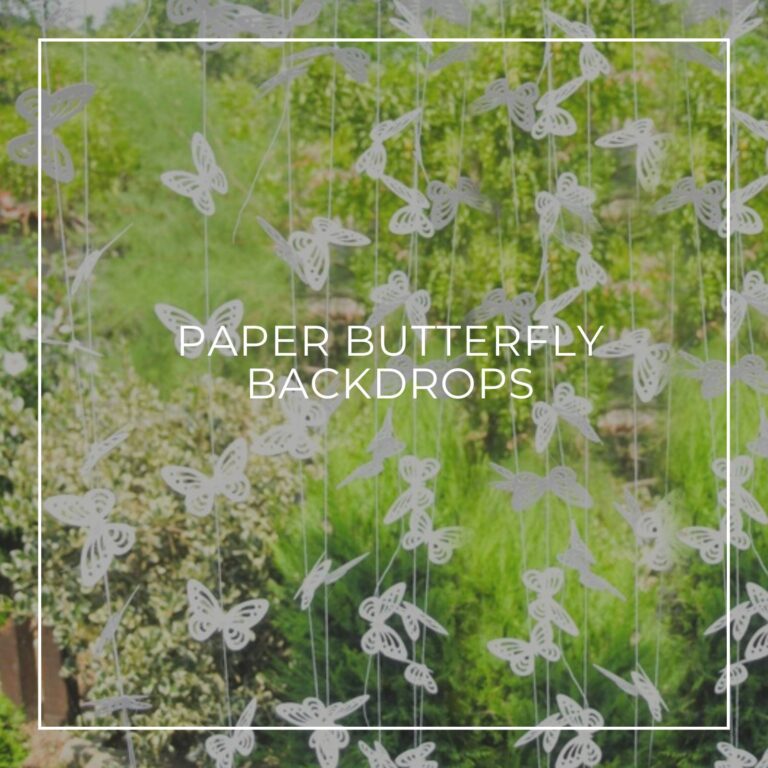 white paper butterfly garland backdrop outside against trees and greenery