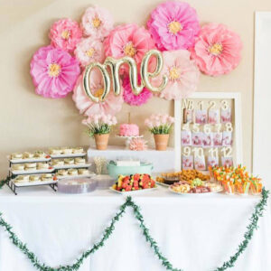 pink paper flower decorations hanging above a 1st birthday party dessert table