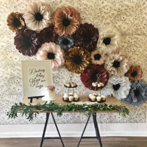 paper flower decorations fixed to the wall above a 1st birthday party dessert table